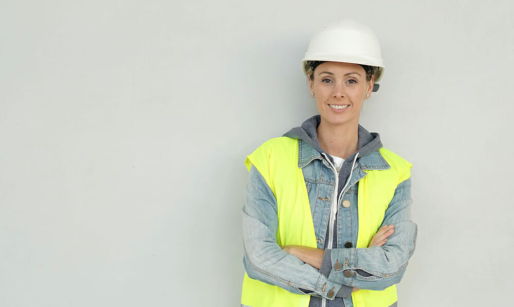 Builderstorm-Smiling female construction worker in safety gear on grey backgr